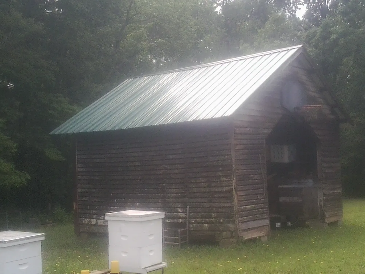Green metal roof on a weathered barn beside stacked beehives in Saint Charles